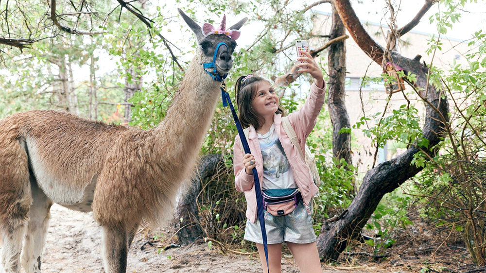 Szenenbild: Die kleine Chanell (rechts im Bild) macht ein Selfie mit einem Lama (links im Bild).
