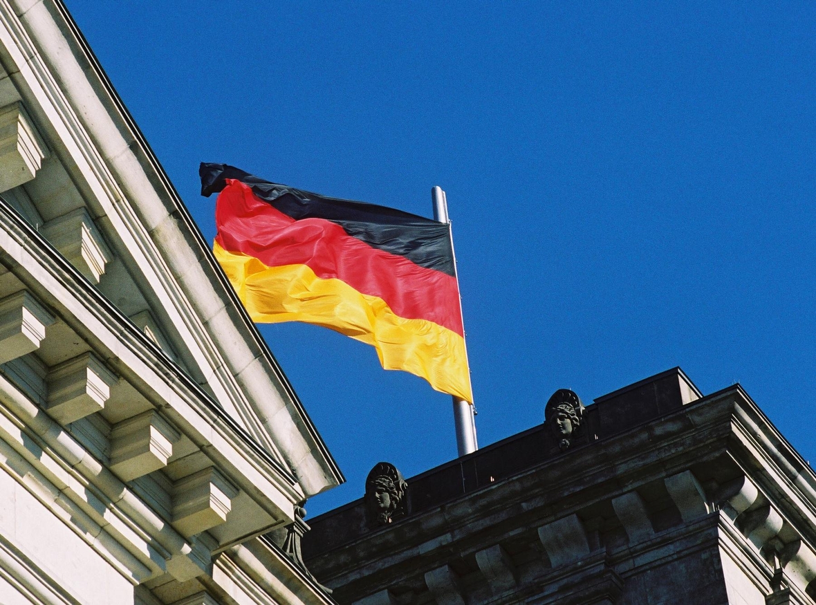 Eine deutsche Flagge in den Farben schwarz-rot-gold weht vor blauem Himmel.