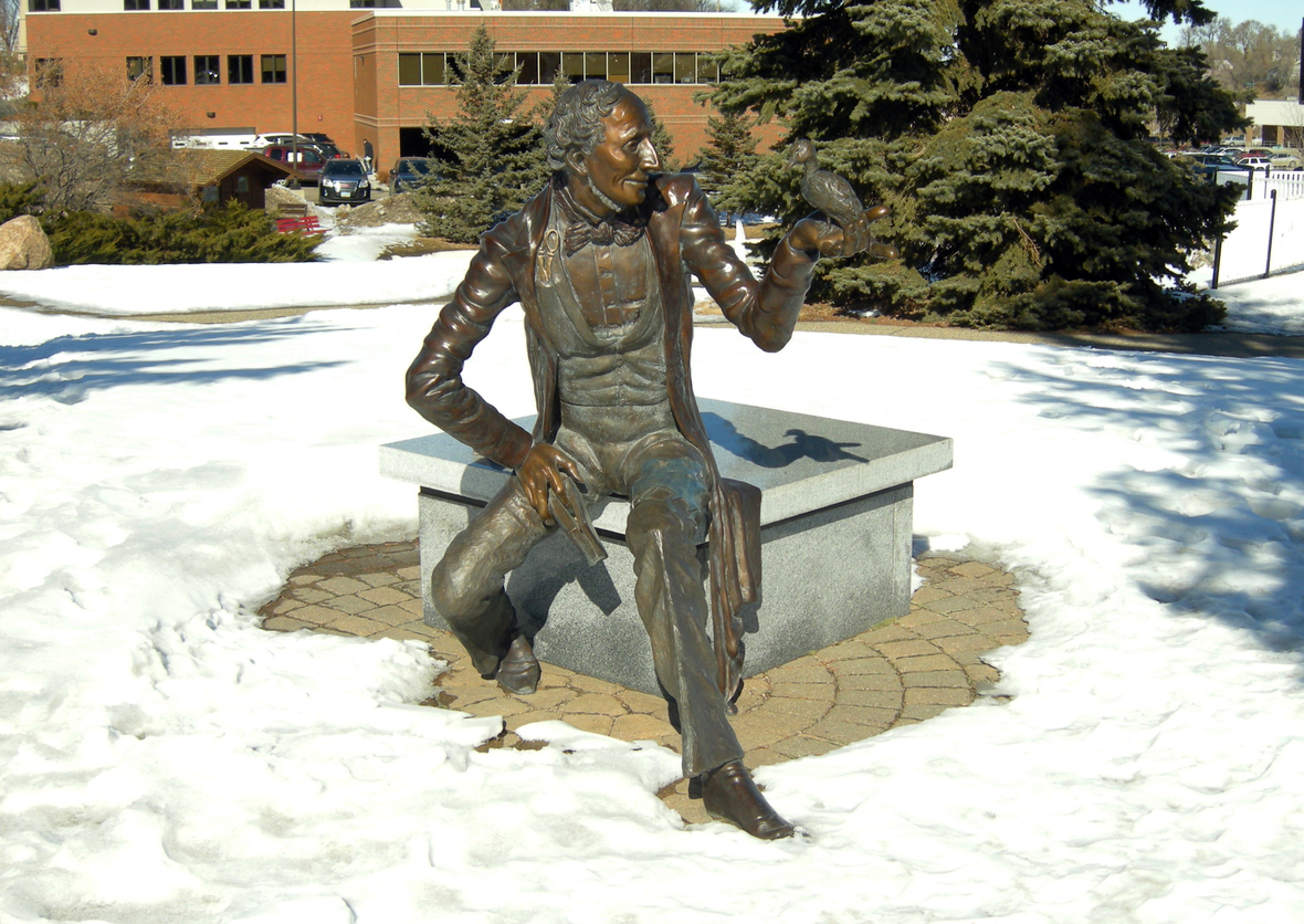 Statue von Hans Christian Andersen im Scandinavian Heritage Park in der US-amerikanischen Stadt Minot. Der Schriftsteller sitzt auf einem Sockel, auf seiner linken Hand sitzt ein Vogel. 