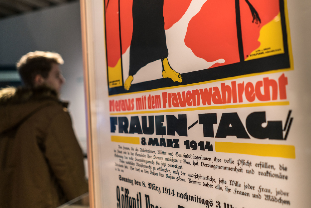 Ein Besucher der Ausstellung "Damenwahl" steht im Historischen Museum Frankfurt hinter einem Plakat zum Frauen-Tag 1914, auf dem "Heraus mit dem Frauenwahlrecht" gefordert wird. 