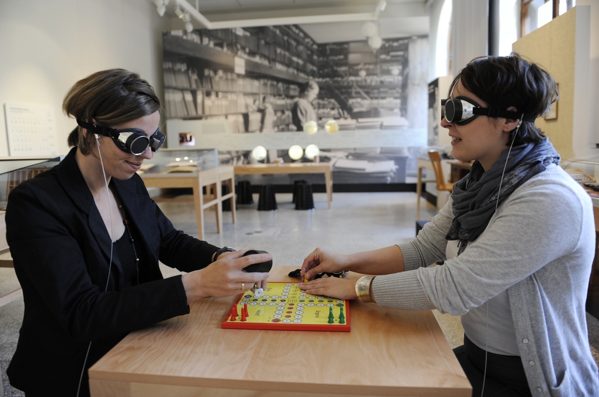 Zwei Frauen spielen in der Ausstellung "Sechs Richtige! Louis Braille und die Blindenschrift" im Museum für Kommunikation in Berlin eine Version des Brettspiels "Mensch ärgere Dich nicht" für Blinde.