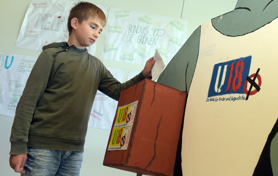 Junge bei einer U18-Wahl wirft Stimmzettel in Wahlurne.