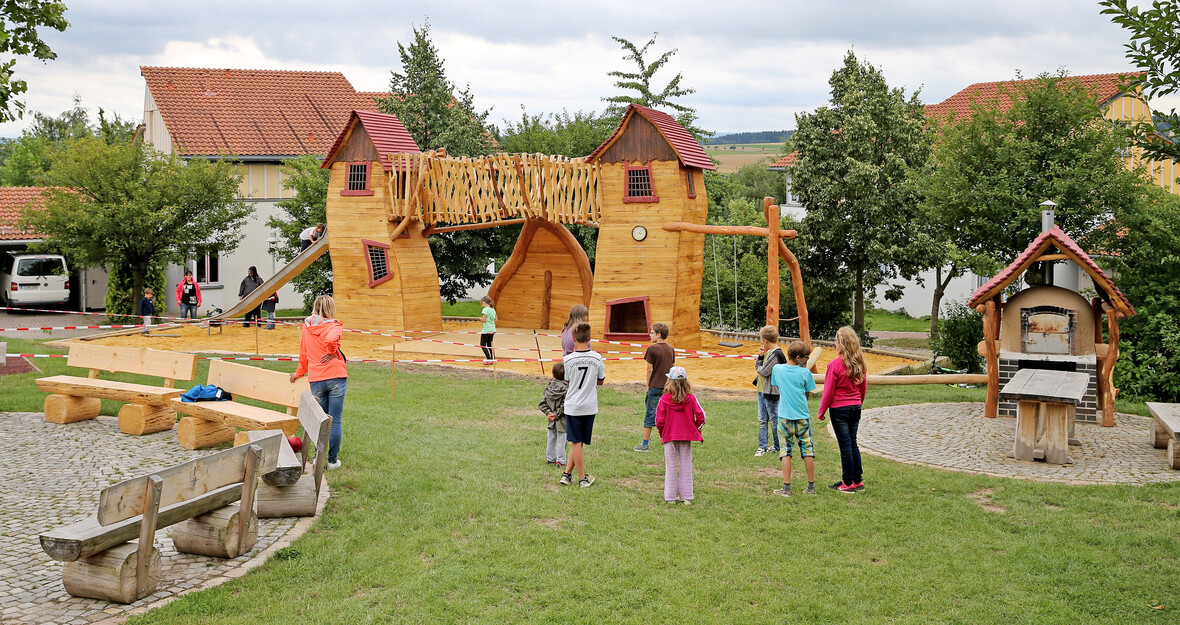 Kinder spielen auf einem großen Abenteuerspielplatz aus Holz mit Kletterbrücke und Rutschen .