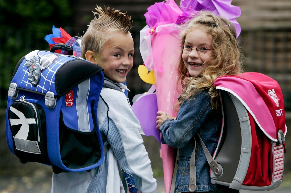 Ein Junge und ein Mädchen gehen mit Schultüten und Schulranzen zur Einschulung.