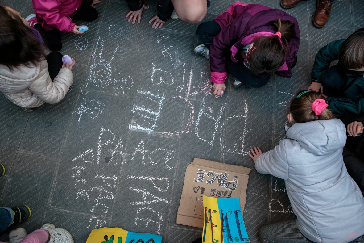 Kinder schreiben das Wort "Peace" (deutsch: Frieden) mit Kreide auf den Boden.