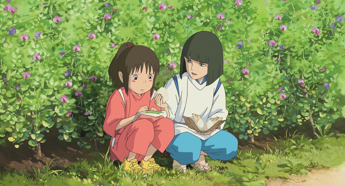Szenenbild: Chihiro und Haku hocken vor einer grünen Hecke und reden miteinander.