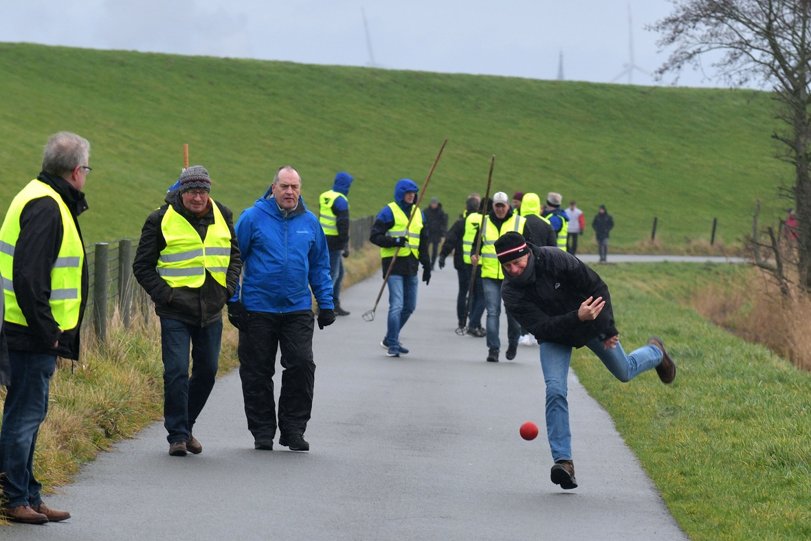 Ein Boßel-Turnier findet in Friesland statt. Eine Person wirft einen roten Boßel-Ball.