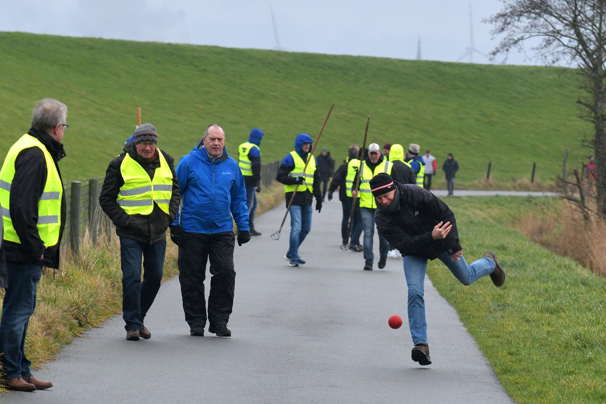 Ein Boßel-Turnier findet in Friesland statt. Eine Person wirft einen roten Boßel-Ball. 