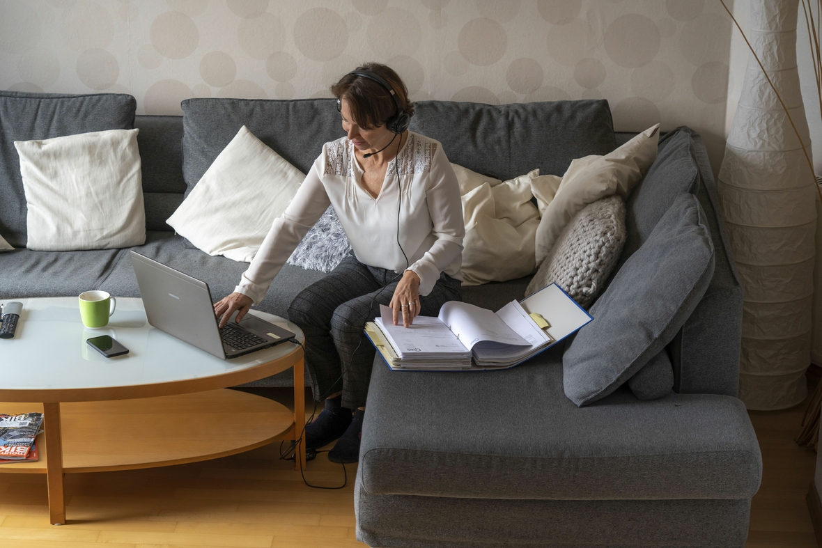 Frau, Mitte 50, arbeitet von Zuhause aus, mit Laptop und kommuniziert per Headset mit Kollegen, Homeoffice, auf dem Sofa