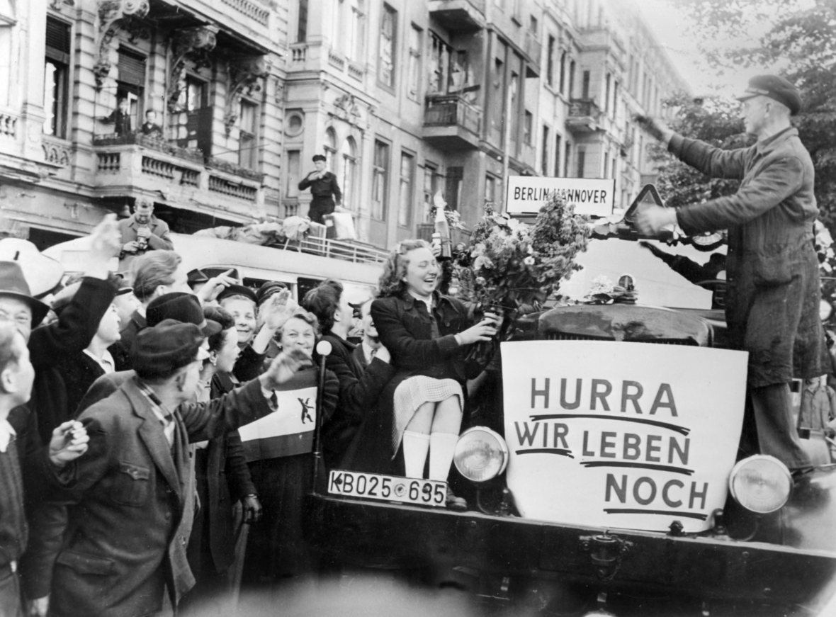 Berliner/innen freuen sich über das Ende der Berlin-Blockade am 12. Mai 1949.  Ein Auto ist mit einem Schild dekoriert auf dem "Hurra wir leben noch" steht. 