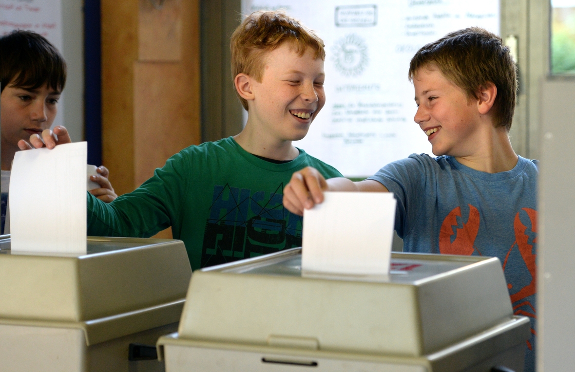 Zwei Schüler aus einer 6. Klasse nehmen an einer U18-Europawahl in ihrer Schule teil. Hier stecken sie ihren Stimmzettel in die Wahlurne.
