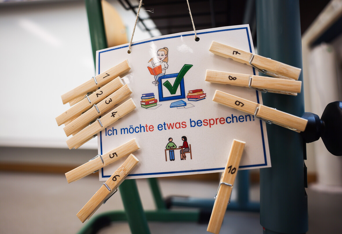 Im Klassenzimmer zeigt ein Schild mit nummerierten Wäscheklammern den Wunsch eines Kindes, etwas zu besprechen. 