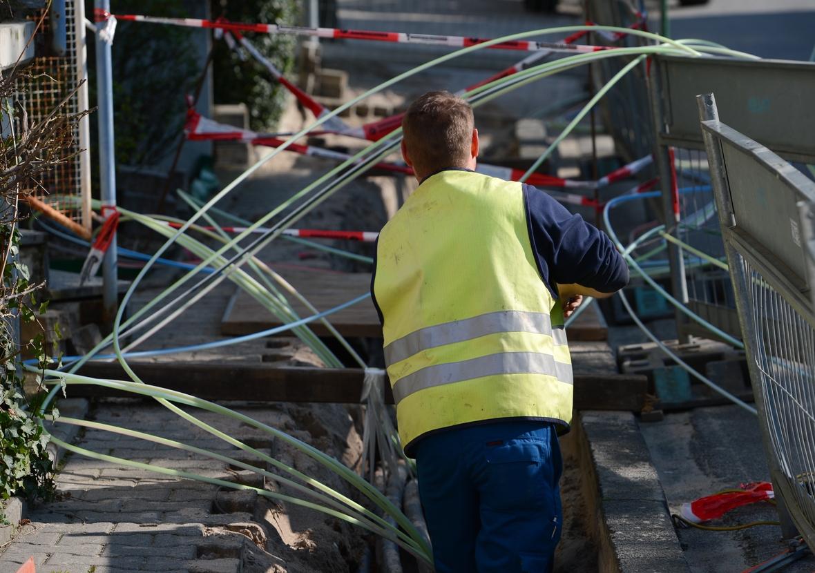 Ein Strommonteur verlegt auf einer Baustelle Erdkabel. In den Leerrohre können Glasfaserkabel und Stromkabel eingezogen werden