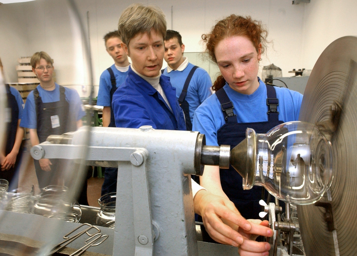 Schüler/innen bei einem Praktikum. Hier sieht man eine junge Frau an einem Schleifapparat. Die Schüler/innen lernen die Glasproduktion in Jena kennen und können selbst ein Werkstück anfertigen.