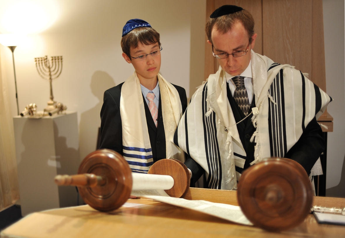 Ein junger Mann feiert in München seine Bar Mizwa. Er schaut mit dem Rabbi die Tora-Rolle an.