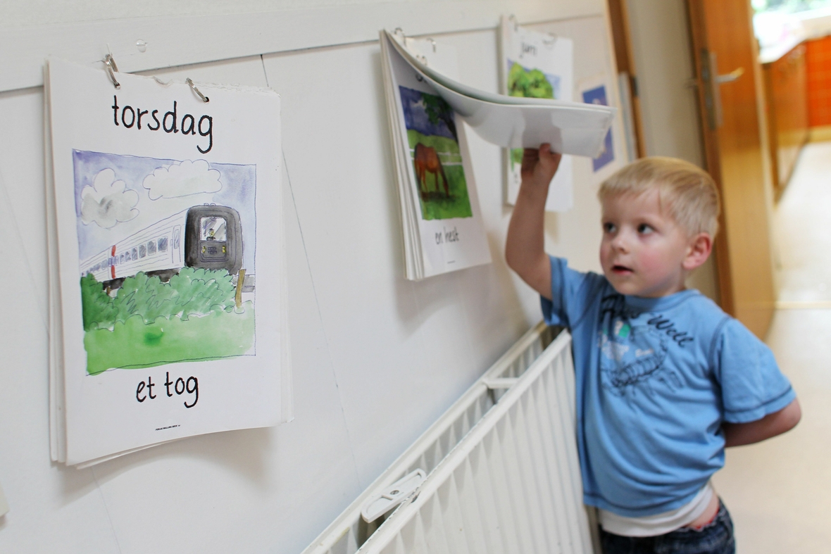Im dänischen Kindergarten in Flensburg steht ein kleiner Junge und schaut sich einen Kalender an, dessen Texte auf Dänisch zu lesen sind.