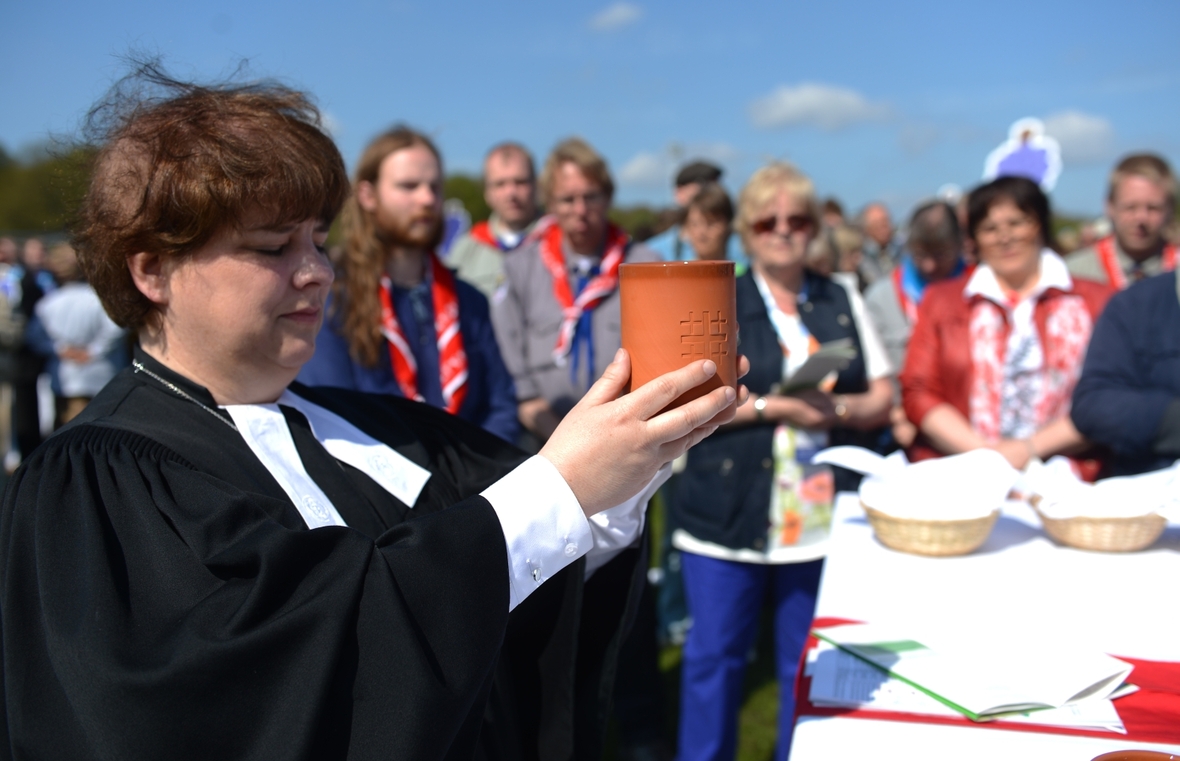 Eine evangelische Pfarrerin feiert beim Kirchentag das Abendmahl. Sie hebt mit den Händen einen Becher.