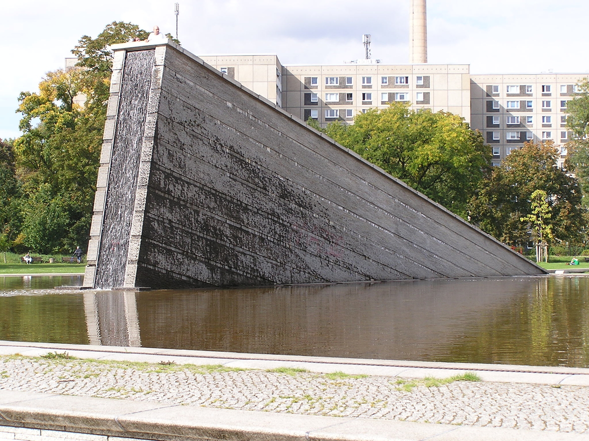 Das Denkmal "Sinkende Mauer" im Invalidenpark in Berlin. Es handelt sich um eine Mauer, die ins Wasser gestürzt ist und  von der nur noch die obere Mauerspitze sichtbar ist.