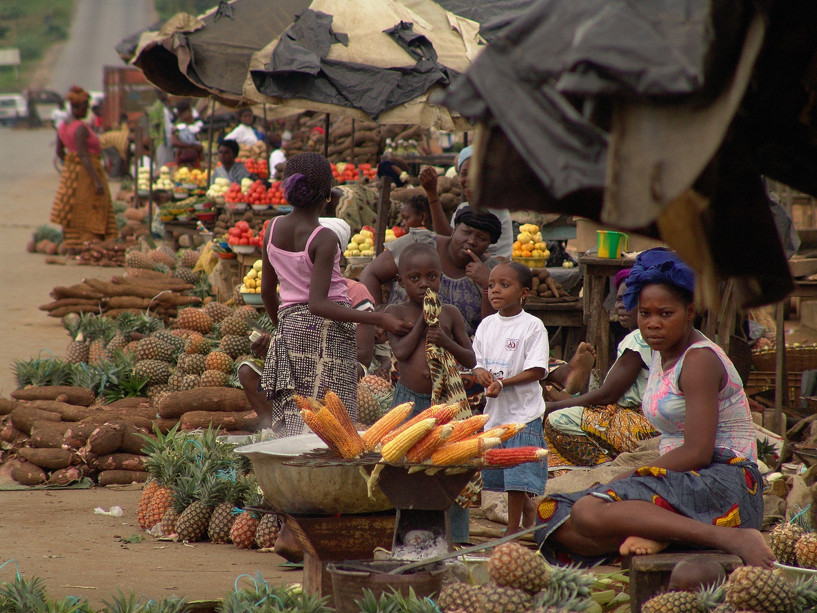 Auf einem traditionellen afrikanischen Markt in der Elfenbeinküste sitzen und stehen Frauen und Kinder zwischen den angebotenen Waren.