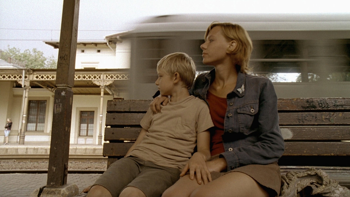 Szenenbild: Stefek, links im Bild, und seine große Schwester Elka sitzen auf einer Bank am Bahnhof