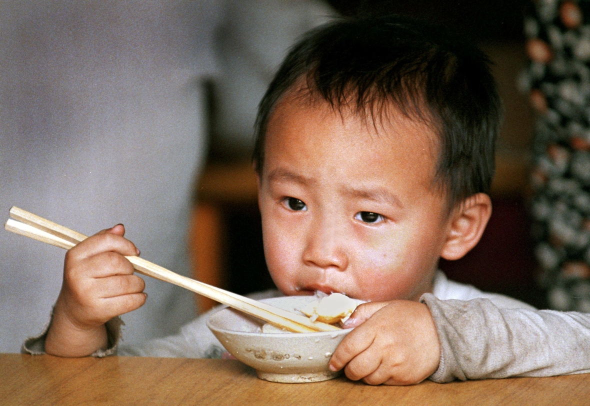 Ein kleiner Junge isst Reis mit Essstäbchen. Reis gehört in China zu den Grundnahrungsmitteln.