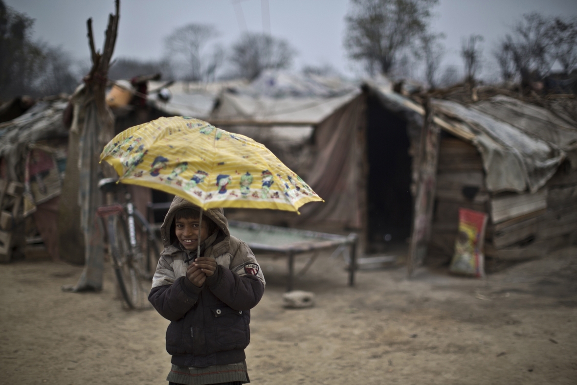 Ein Junge in den Slums von Islamabad, Pakistan. Im Regen umklammert er lächelnd einen Regenschirm.
