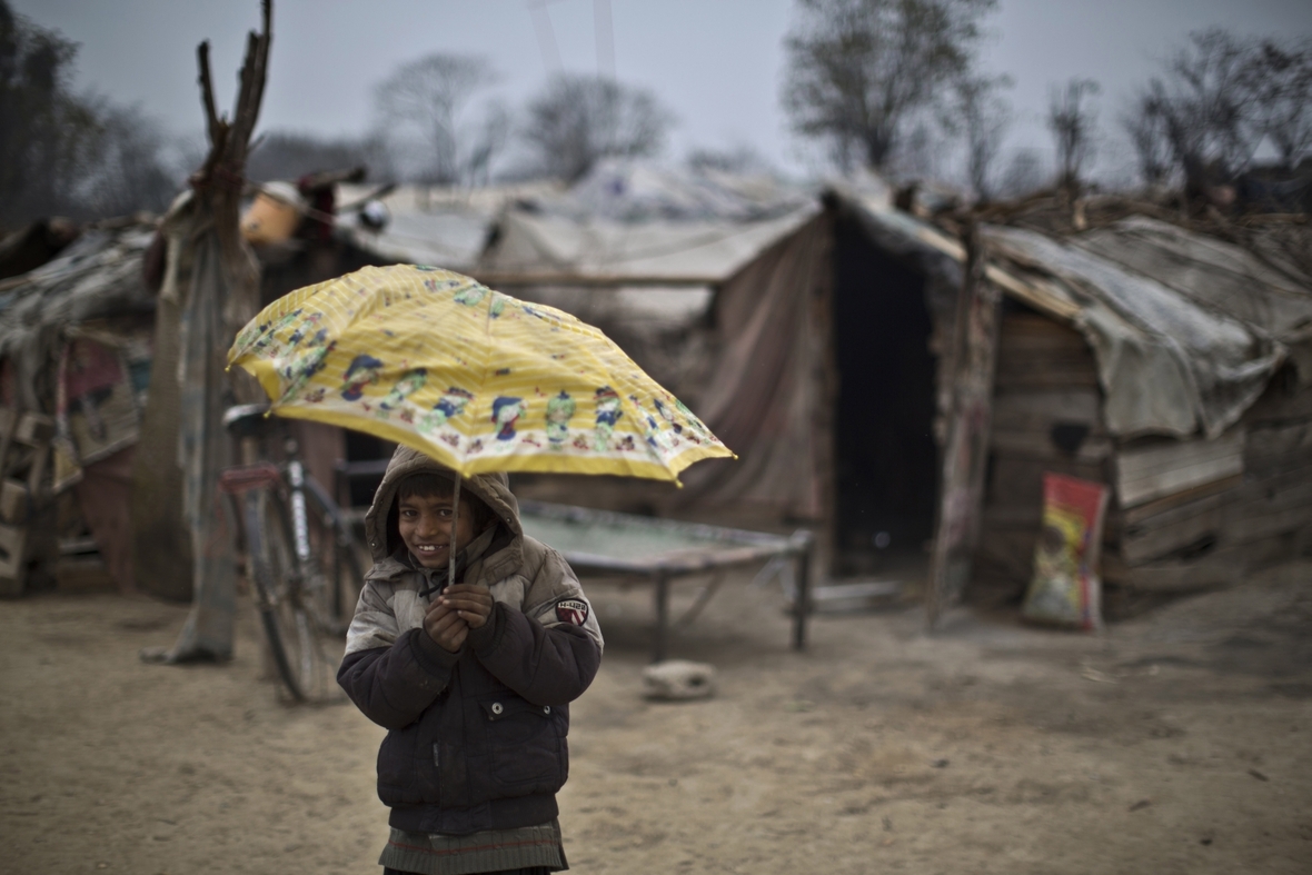 Ein Junge in den Slums von Islamabad, Pakistan. Im Regen umklammert er lächelnd einen Regenschirm.
