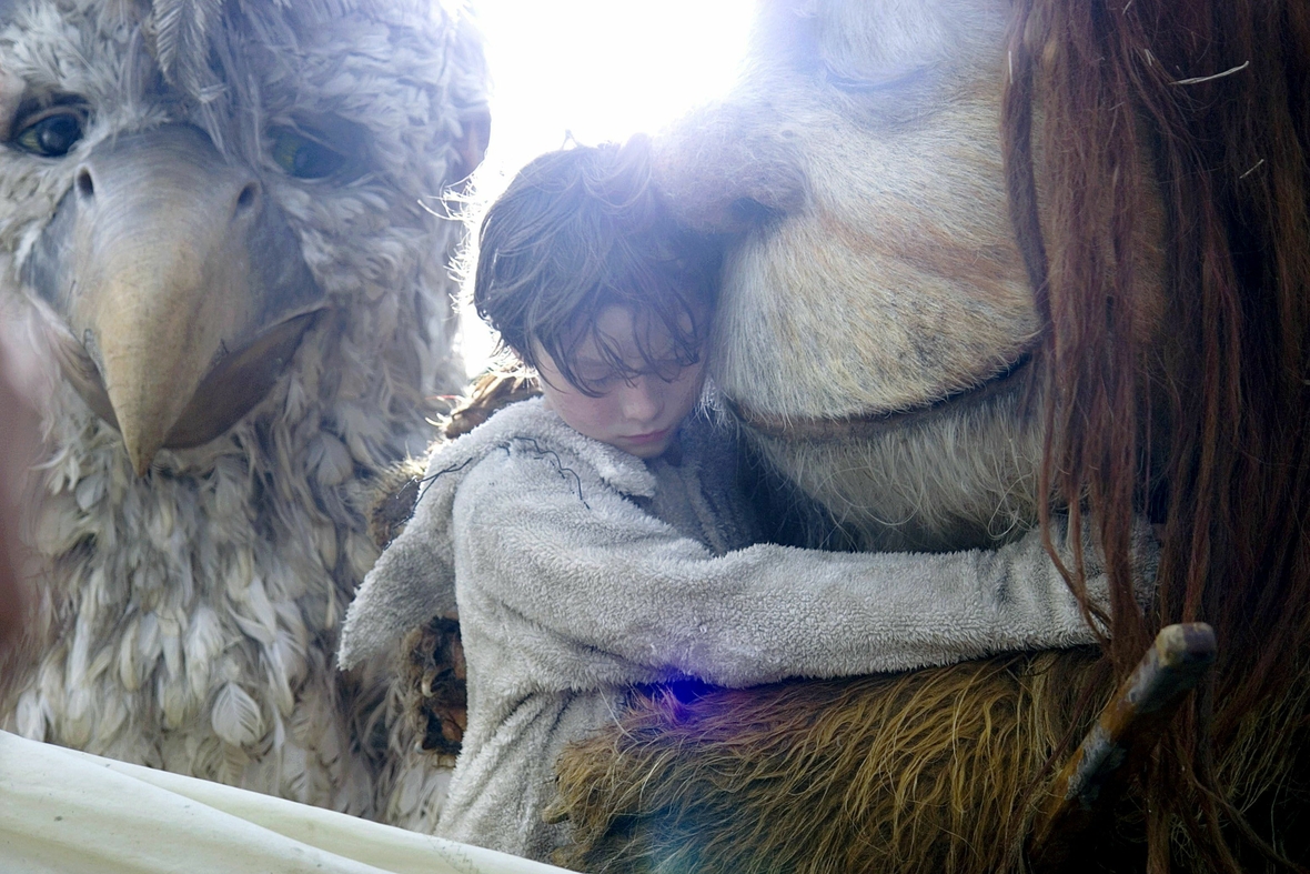Szenenbild: Max zwischen zwei wilden Kerlen, die aussehen wie große Tiere.  Max umarmt den rechts von ihm stehenden wilden Kerl liebevoll.