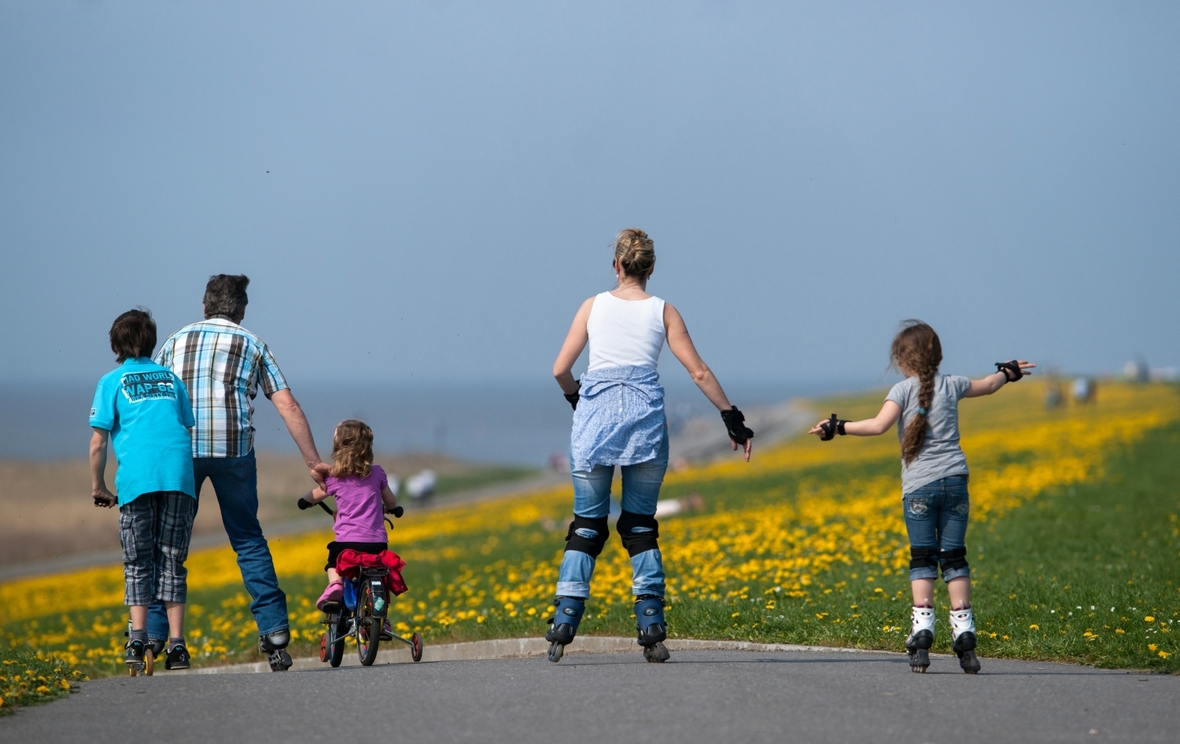 Ein Mann, eine Frau und drei Kinder fahren mit Inline-Skates, Fahrrad und Tretroller den Deich hinunter. Weltweit wird an verschiedenen Aktionstagen im Jahr an die Rechte, Bedürfnisse, aber auch die Nöte von Kindern erinnert. Am 1. Juni ist Internationaler Kindertag.