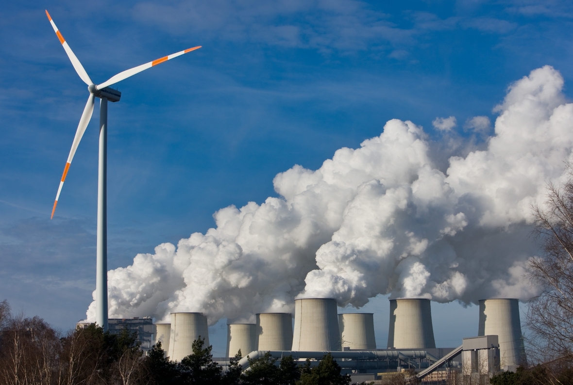 In Jänschwalde in Brandenburg stoßen alte und neue Methoden der Energiegewinnung aufeinander. Ein Windrad dreht sich vor den Kühltürmen des Braunkohlekraftwerks.