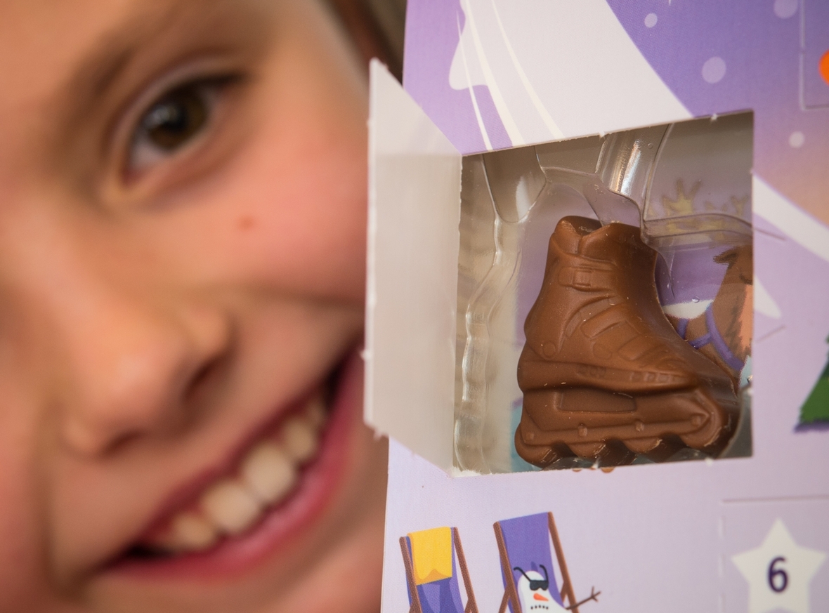 Ein Mädchen freut sich über ein geöffnetes Türchen eines Adventskalenders. Der Adventskalender ist mit Schokolade gefüllt.