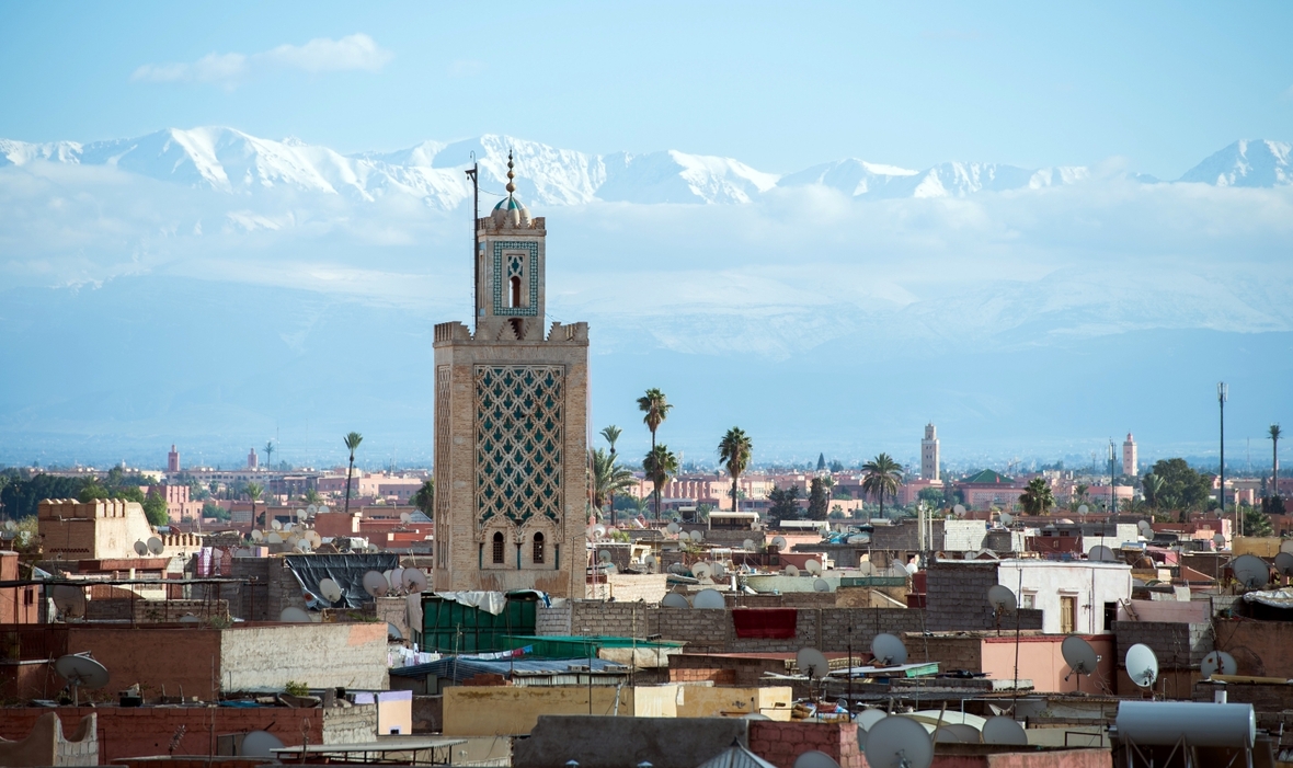 Die marokkanische Stadt Marrakesch mit der Koutoubia-Moschee und dem Atlas Gebirge im Hintergrund.