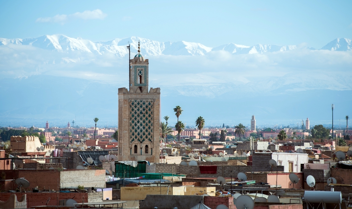 Die marokkanische Stadt Marrakesch mit der Koutoubia-Moschee und dem Atlas Gebirge im Hintergrund.


