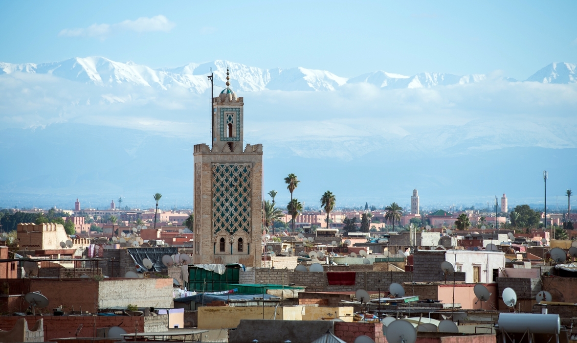 Die marokkanische Stadt Marrakesch mit der Koutoubia-Moschee und dem Atlas Gebirge im Hintergrund.

