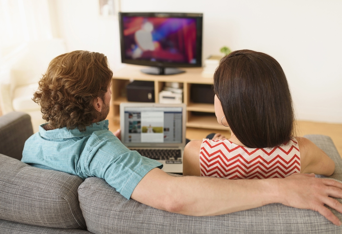 Ein Paar nutzt Fernseher und Laptop