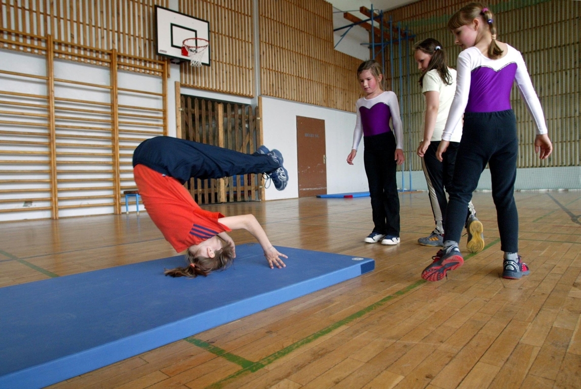 Sportunterricht in einer Schule. Kinder machen eine Rolle vorwärts beim Bodenturnen