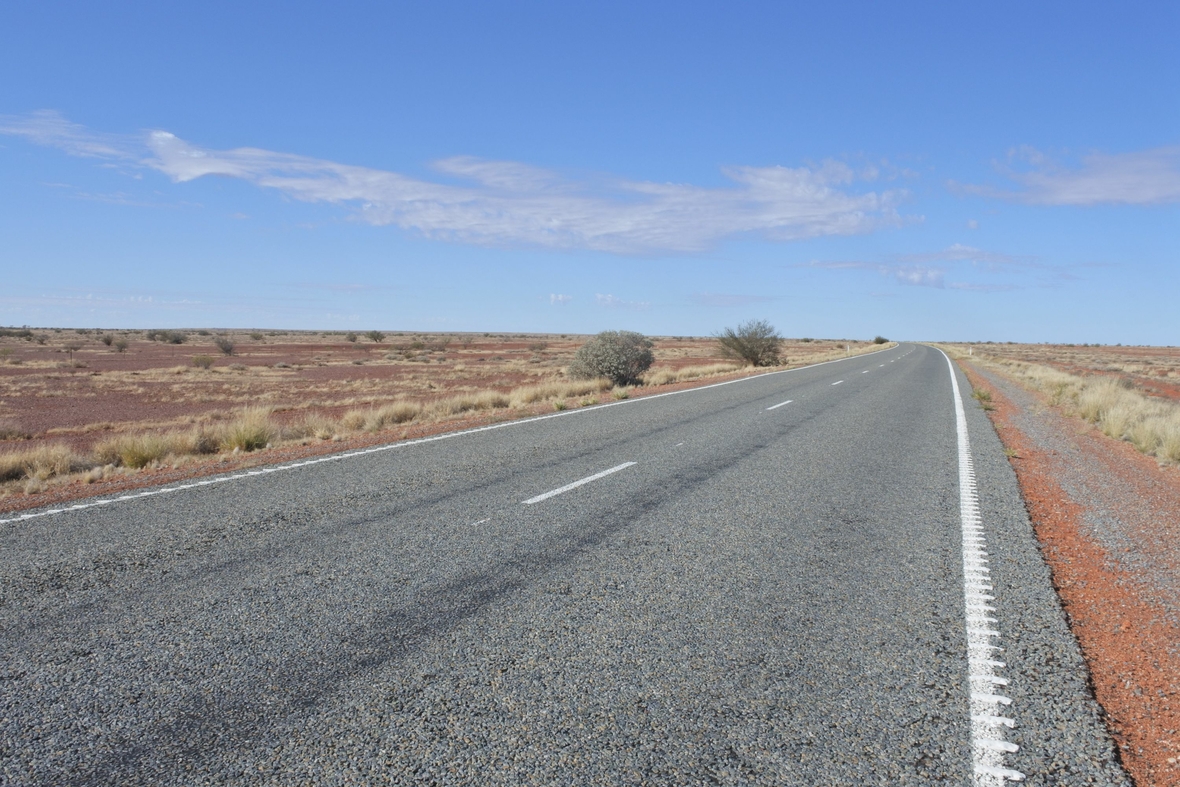 Eine lange, leere Autostraße ohne Häuser, Tankstellen oder anderen Gebäuden im australischen Outback.