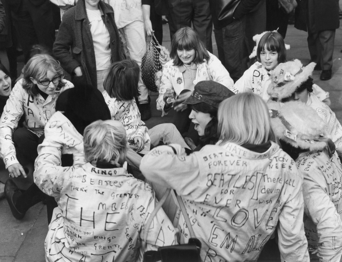 Eine Gruppe junger Mädchen sitzt am 26.10.1965 vor dem Buckingham Palastes in London. Die britische Popgruppe wurde an diesem Tag von der Queen mit einem Orden  ausgezeichnet. Aus diesem Grund hatten sich vor dem Königspalast zahlreiche Fans eingefunden, die zum Teil selbstbemalte Hemden mit den Namen ihrer Idole trugen.