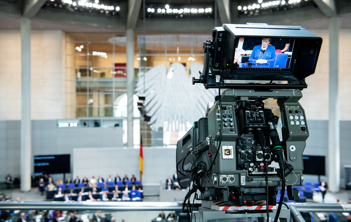 Ein Kameraobjektiv zeigt im Bundestag die Befragung von Bundeskanzlerin Angela Merkel bei einer aktuellen Stunde.